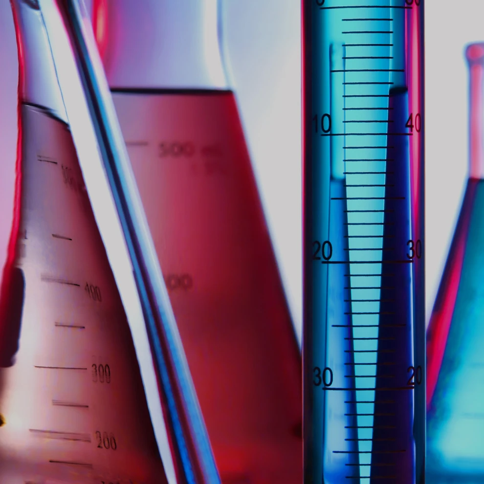 Close-up shot of several beakers and test tubes. They are filled with pink and blue liquid.