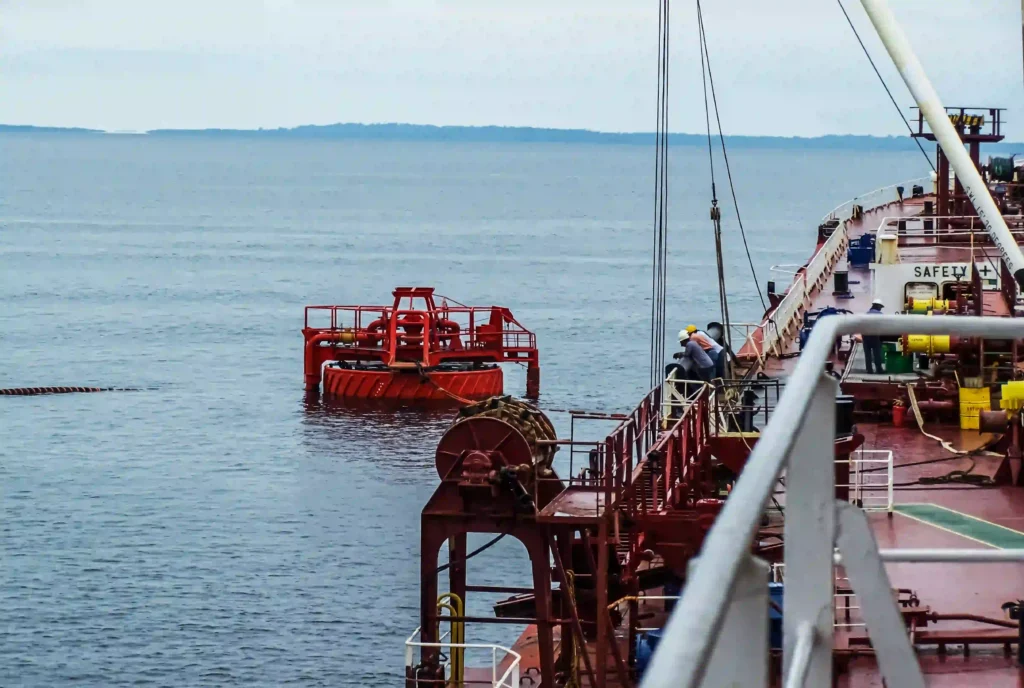 A floating hose string and mooring buoy alongside a tanker during an offshore transfer.
